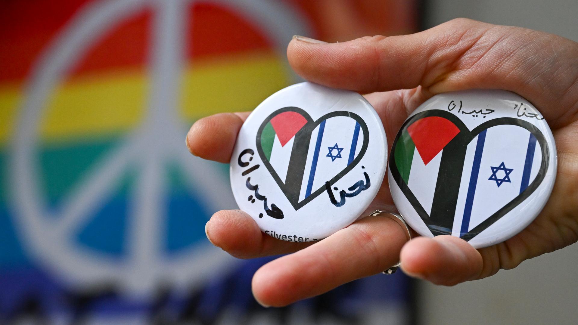 Ein Hand hält Buttons mit einem Herz, auf dem die israelische und palestinensische Flagge zu sehen ist