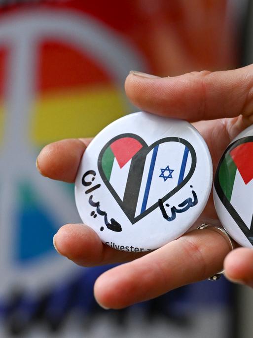 Ein Hand hält Buttons mit einem Herz, auf dem die israelische und palestinensische Flagge zu sehen ist