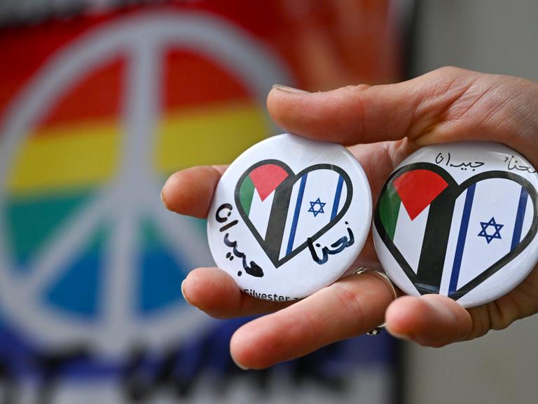 Ein Hand hält Buttons mit einem Herz, auf dem die israelische und palestinensische Flagge zu sehen ist