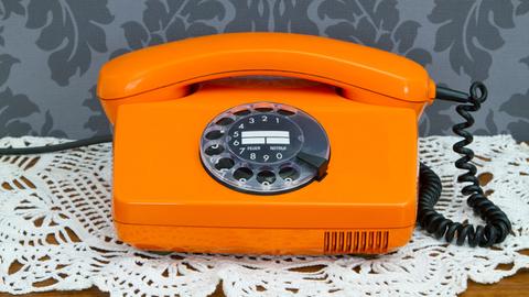 Ein altes orangenes Telefon mit Wählscheibe.
