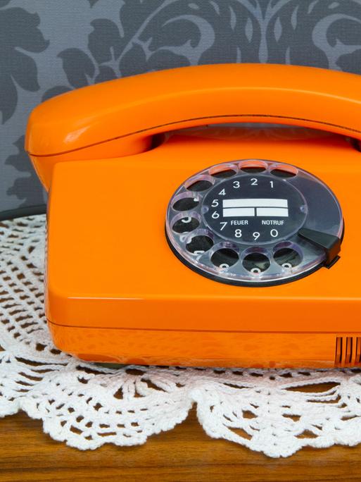 Ein altes orangenes Telefon mit Wählscheibe.
