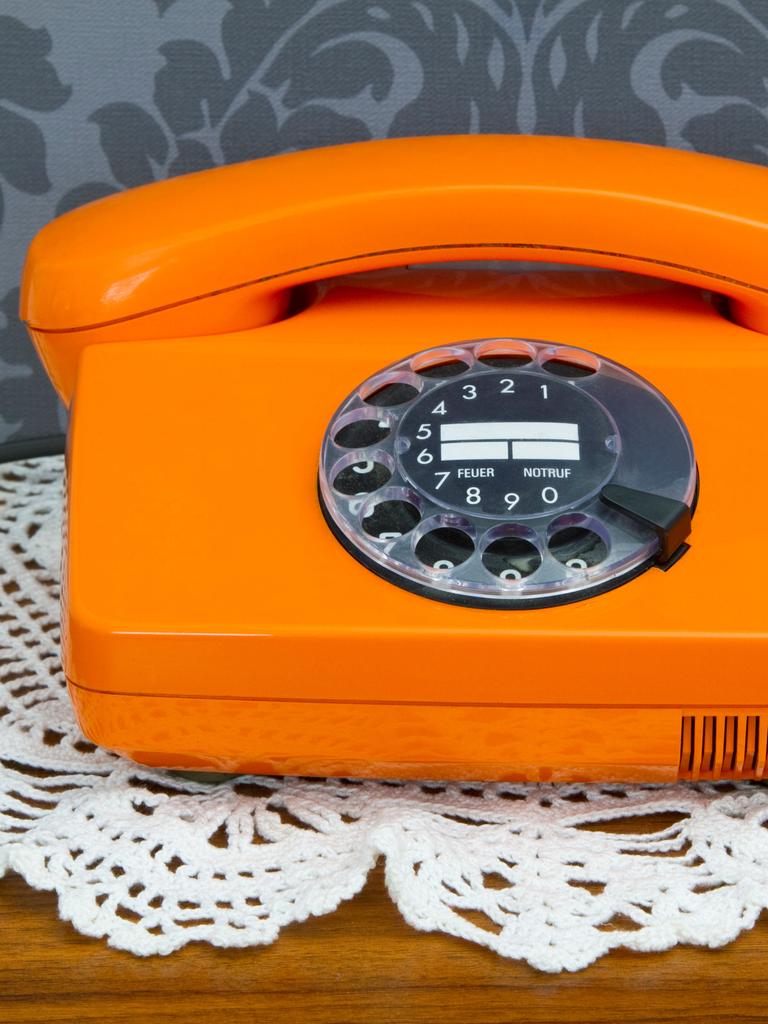 Ein altes orangenes Telefon mit Wählscheibe.