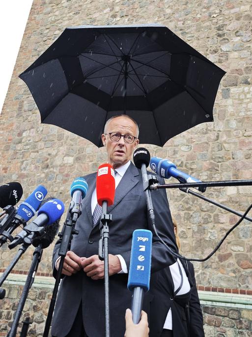 Bundeskanzler Friedrich Merz CDU steht unter einem Regenschirm vor Mikrofonen und spricht Bundeskanzler Friedrich Merz CDU steht unter einem Regenschirm vor Mikrofonen und spricht