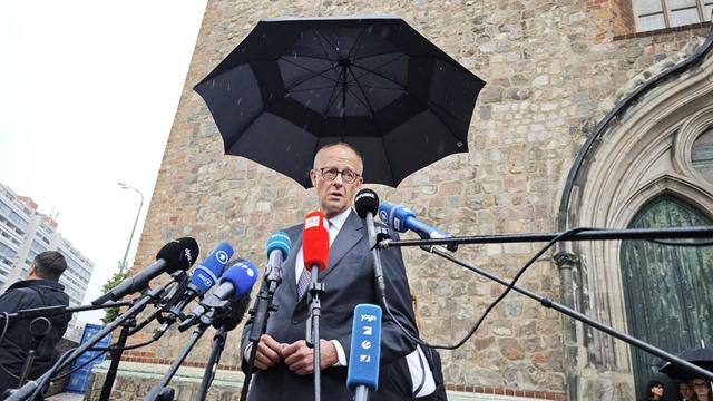 Bundeskanzler Friedrich Merz CDU steht unter einem Regenschirm vor Mikrofonen und spricht