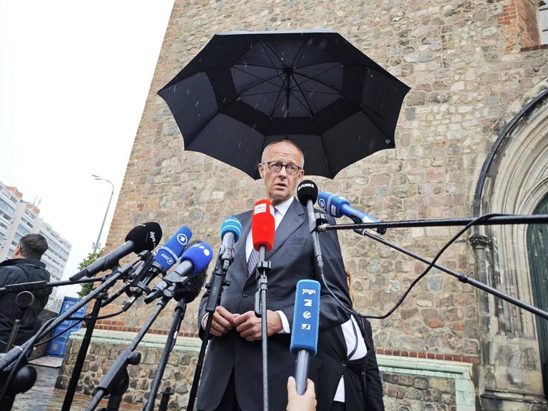 Bundeskanzler Friedrich Merz CDU steht unter einem Regenschirm vor Mikrofonen und spricht Bundeskanzler Friedrich Merz CDU steht unter einem Regenschirm vor Mikrofonen und spricht