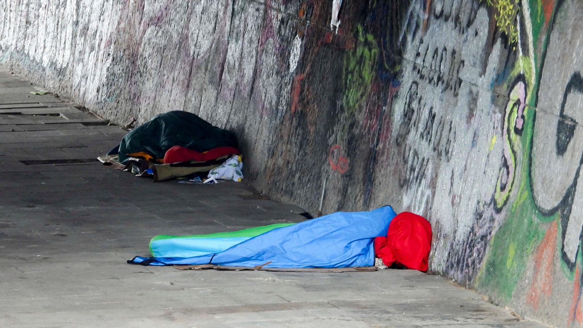 Obdachlose schlafen in bunten Schlafsäcken unter einer Brücke in Hamburg.