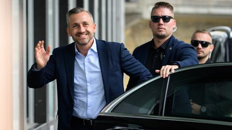 Ulrich Siegmund, AfD-Spitzenkandidat in Sachsen-Anhalt, steigt aus einem Wagen und winkt in die Kamera, hinter ihm stehen zwei Personenschützer mit dunklen Sonnenbrillen.