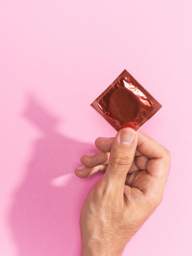 Eine Hand hält eine geschlossene Kondompackung vor einem rosa Hintergrund.