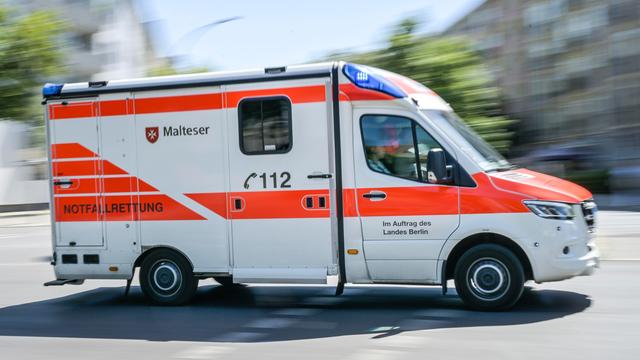 Das Foto zeigt einen Kranken-Wagen. Er fährt über eine Straße in der Stadt Berlin.