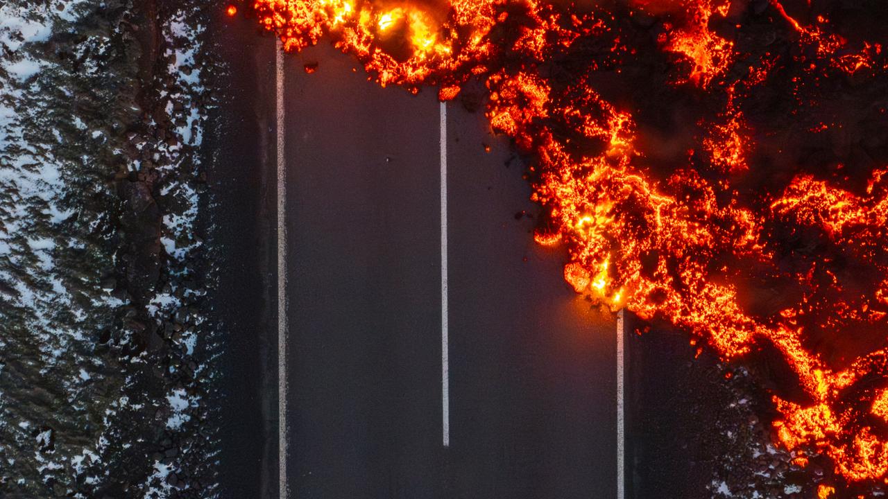 Die glühende Lava eines Vulkanausbruches auf Island läuft über eine asphaltierte Landstraße