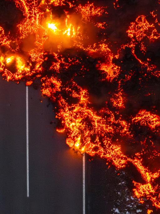 Die glühende Lava eines Vulkanausbruches auf Island läuft über eine asphaltierte Landstraße