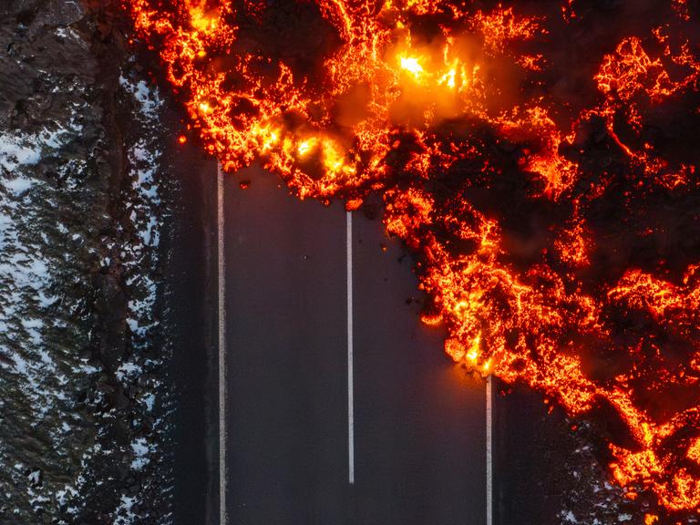 Die glühende Lava eines Vulkanausbruches auf Island läuft über eine asphaltierte Landstraße