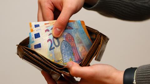 Hände ziehen einige Geldscheine aus einem Portemonnaie.