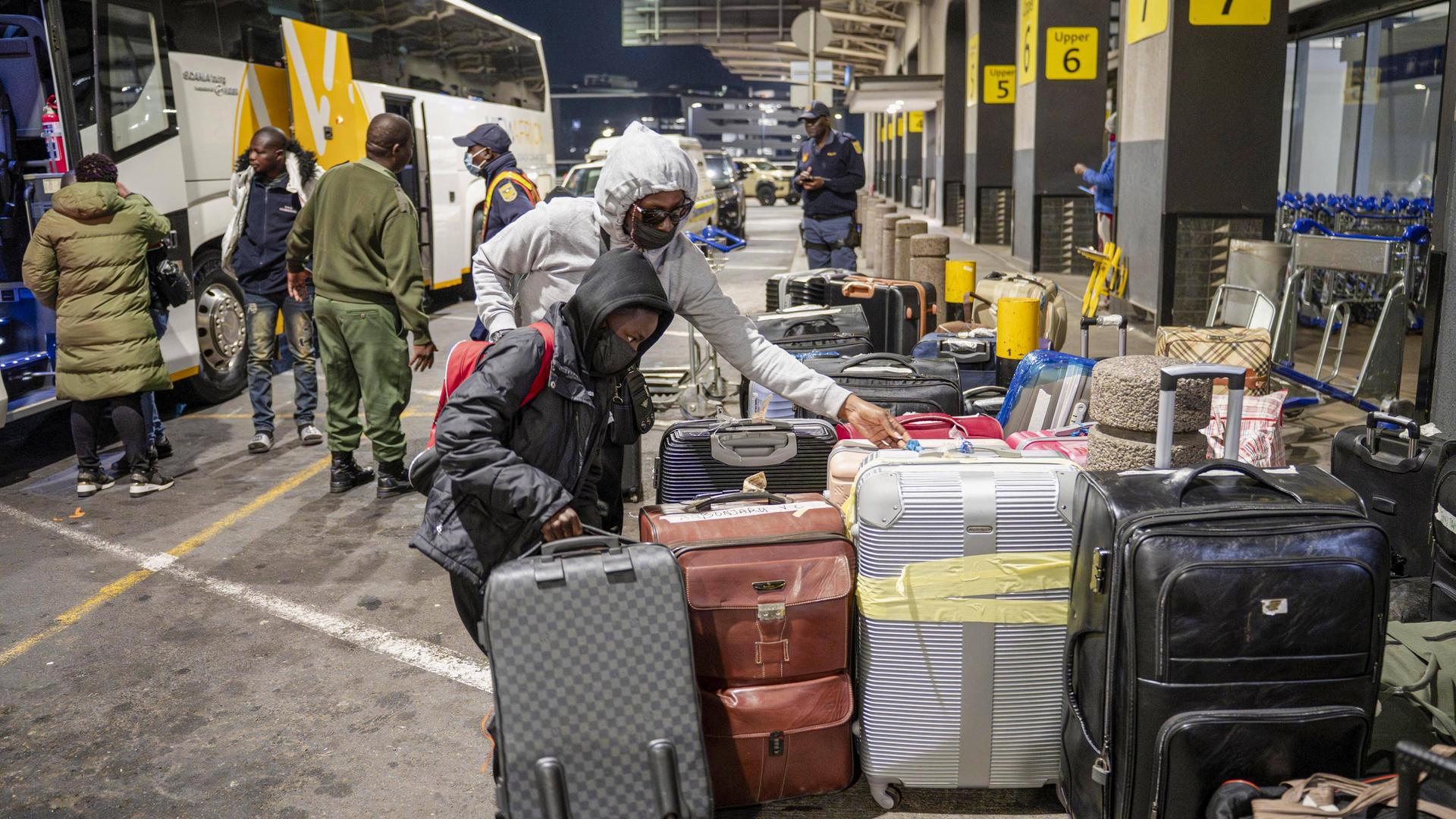 Menschen stehen neben Gepäck in Johannesburg neben Bussen, um zum Oliver Reginald Tambo International Airport gebracht zu werden.