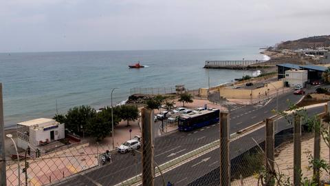 Blick vom Grenzzaun auf Teile der spanische Stadt Ceuta. Zu sehen ist eine Straße an der Küste. Im Hintergrund ist das Mittelmeer zu sehen. 