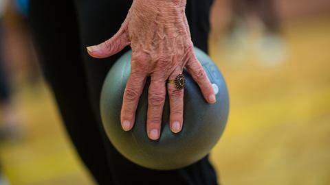 Eine Seniorin macht in der Seniorengymnastik Übung mit dem Ball. 