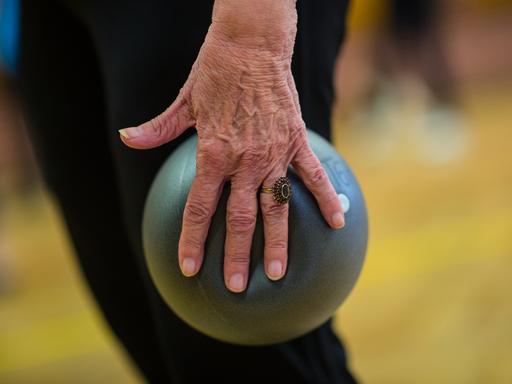 Eine Seniorin macht in der Seniorengymnastik Übung mit dem Ball. 