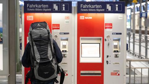 Ein Fahrgast mit großem Rucksack steht in einem Fernbahnhof vor einem Fahrkartenautomaten. 