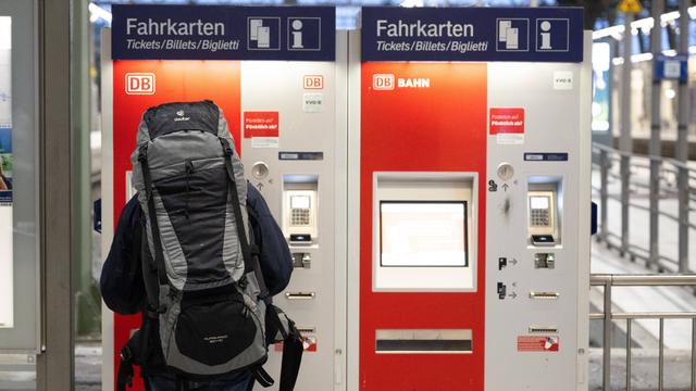 Eine Person steht vor einem Automaten für Fahr-Karten. Sie trägt einen großen Ruck-Sack.