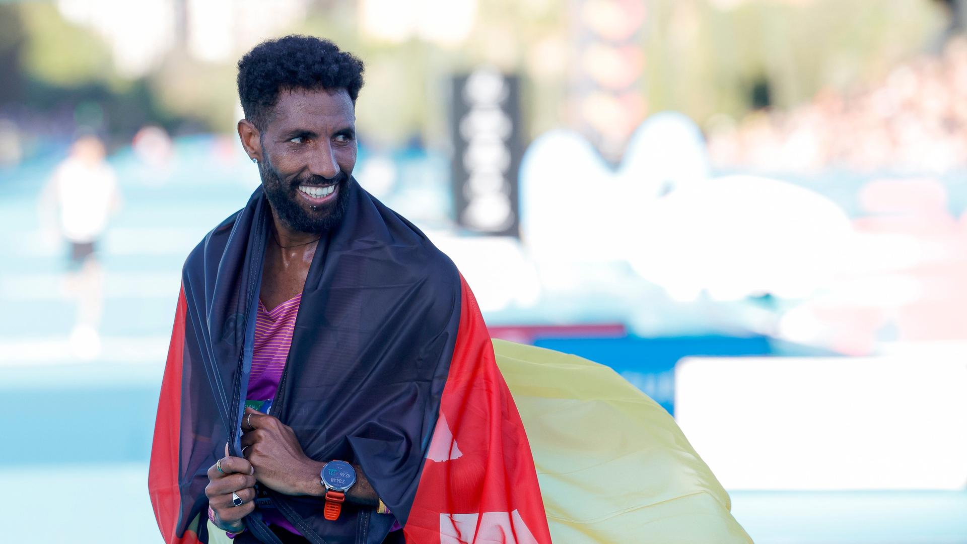 Marathonläufer Amanal Petros hat sich eine Deutschlandfahne um die Schulter gelegt und lächelt. 