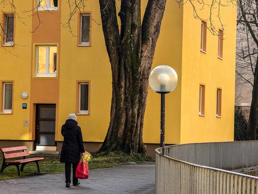 Eine alte Frau läuft alleine durch ein städtisches Wohnviertel. Sie trägt eine Einkaufstüte in der Hand. (Symbolbild)