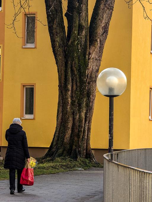 Eine alte Frau läuft alleine durch ein städtisches Wohnviertel. Sie trägt eine Einkaufstüte in der Hand. (Symbolbild)