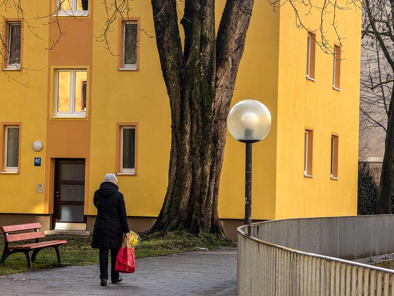 Eine alte Frau läuft alleine durch ein städtisches Wohnviertel. Sie trägt eine Einkaufstüte in der Hand. (Symbolbild)