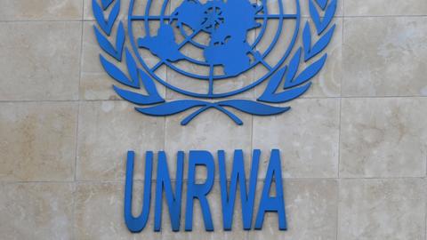 Das blaue Logo der UNWRA vor einer grauen Hauswand