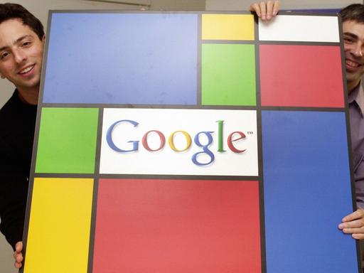Zwei etwa 30-jährige Männer halten lachend eine farbige Tafel mit dem Firmenlogo "Google" hoch.