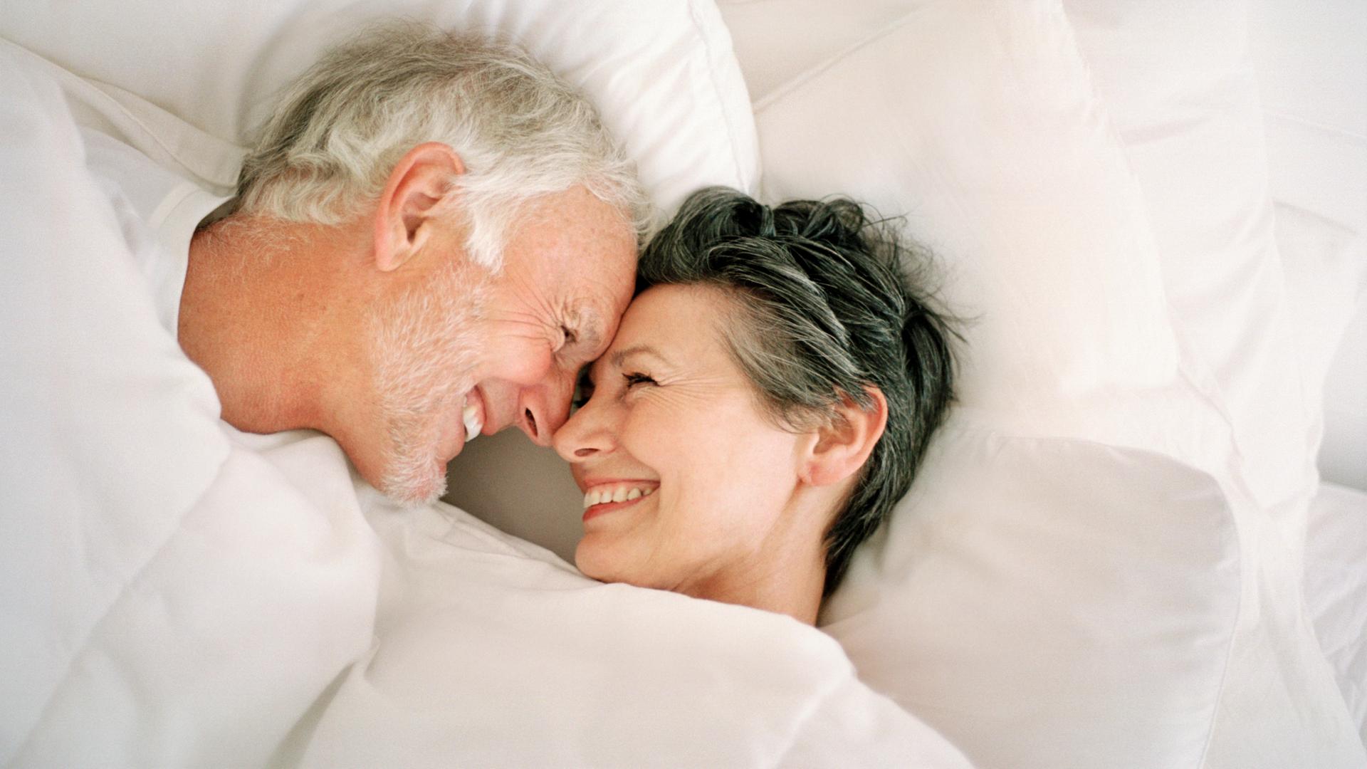 Ein älteres Paar lacht einander im Bett an.