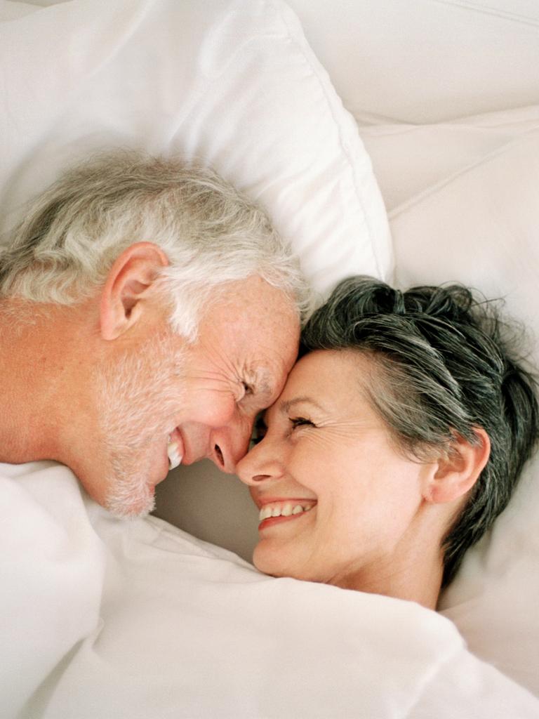 Ein älteres Paar lacht einander im Bett an.