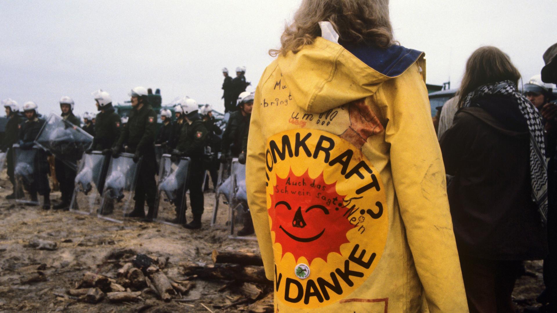 Eine Frau mit einem gelben Regenmantel und der Aufschrift "Atomkraft, nein danke!" ist zu sehen im Hüttendorf in Gorleben, 1980.