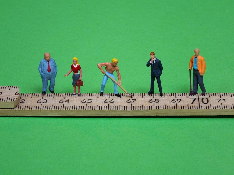 Figuren auf einem Zollstock. Ihr Standort markiert das jeweilige Rentenalter.