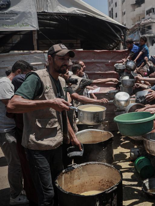 Palästinenser im Gazastreifen drängen sich an einer Essensausgabe und halten leere Schüsseln in der Hand.