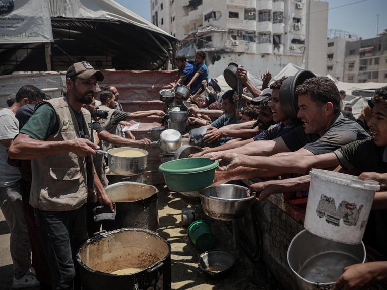 Palästinenser im Gazastreifen drängen sich an einer Essensausgabe und halten leere Schüsseln in der Hand.