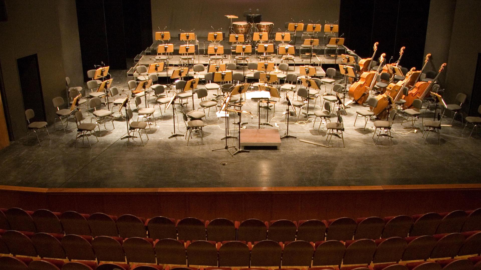 Publikum sitzt vor einer Bühne mit leeren Orchesterstühlen. Publikum sitzt vor einer Bühne mit leeren Orchesterstühlen.