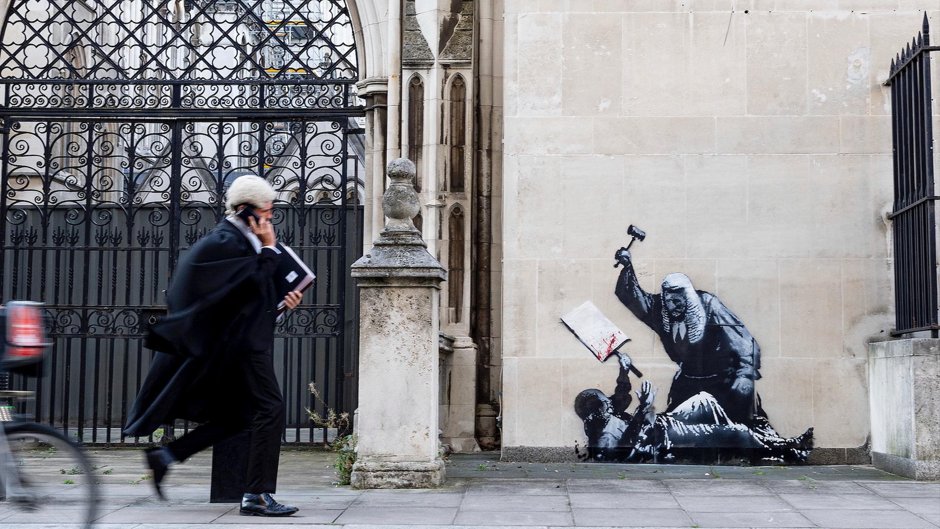 Das Foto zeigt ein Kunstwerk von Banksy. Zu sehen ist ein Richter, der einen Demonstranten im Royal Courts of Justice in London mit einem Hammer schlägt. Das Foto zeigt ein Kunstwerk von Banksy. Zu sehen ist ein Richter, der einen Demonstranten im Royal Courts of Justice in London mit einem Hammer schlägt.