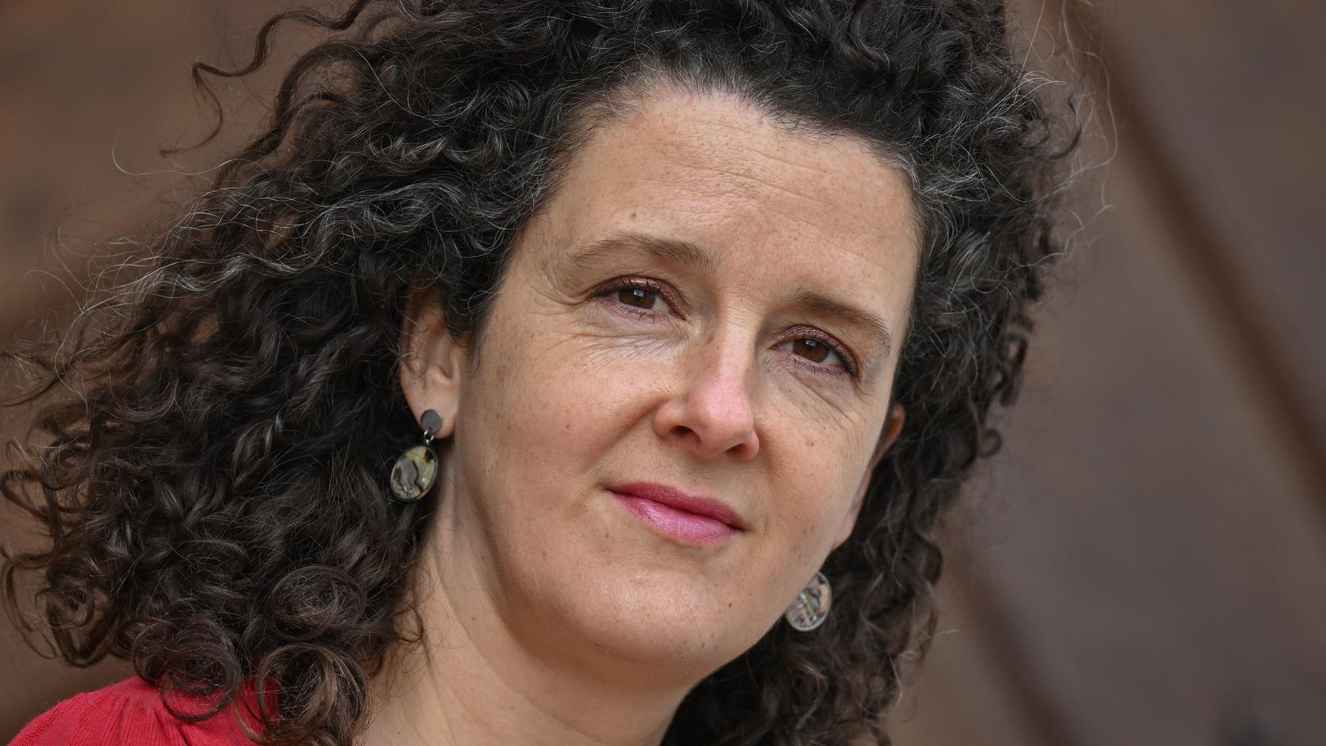 Franziska Hauser trägt offene lockige Haare und ein rotes Oberteil und schaut freundlich in die Kamera. Franziska Hauser trägt offene lockige Haare und ein rotes Oberteil und schaut freundlich in die Kamera.