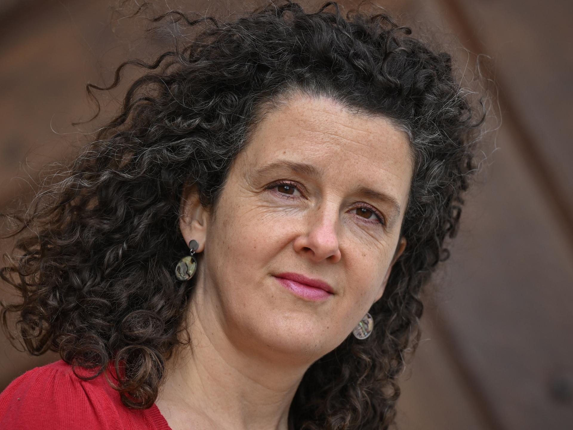 Franziska Hauser trägt offene lockige Haare und ein rotes Oberteil und schaut freundlich in die Kamera.