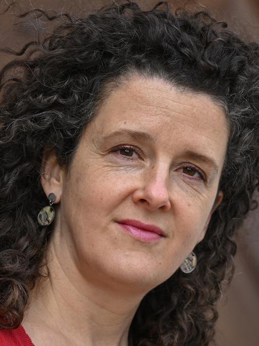 Franziska Hauser trägt offene lockige Haare und ein rotes Oberteil und schaut freundlich in die Kamera.