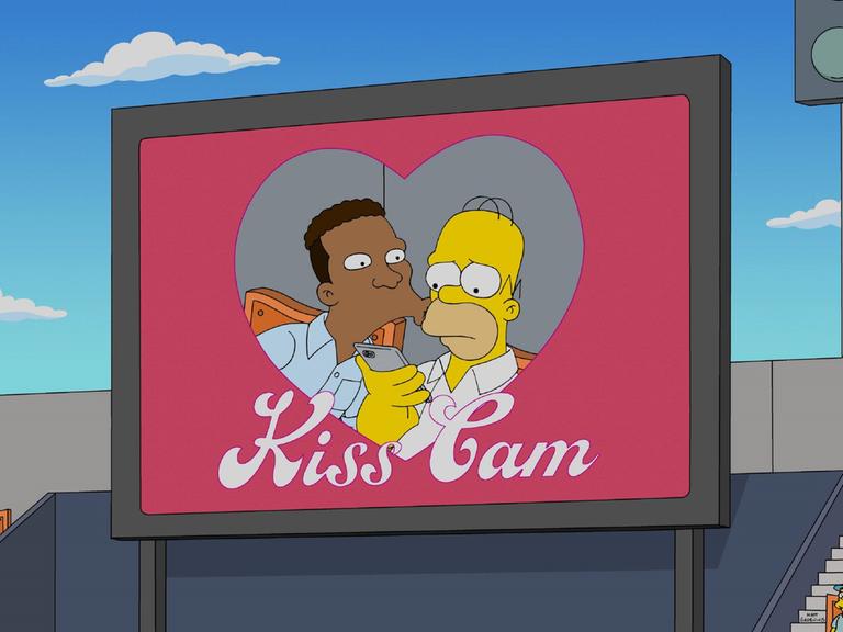 Zu sehen ist eine Leinwand in einem Stadion, unter der "Kiss-Cam" (deutsch: Kuss-Kamera) steht. Homer Simpson bekommt auf der Leinwand einen Kuss von Carl Carlson, schaut aber etwas bedröppelt. 