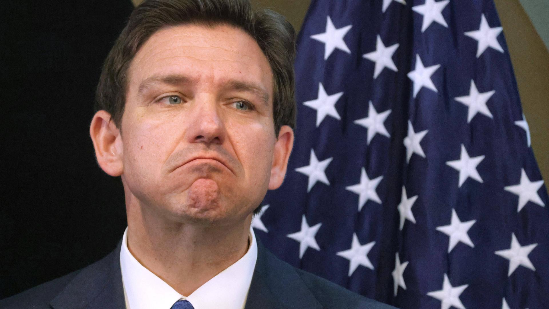 Ronald "Ron" DeSantis blickt mit entschlossenem Gesichtsausdruck ins Off der Kamera. Hinter ihm ist eine US-amerikanische Flagge zu sehen. Ronald "Ron" DeSantis blickt mit entschlossenem Gesichtsausdruck ins Off der Kamera. Hinter ihm ist eine US-amerikanische Flagge zu sehen.