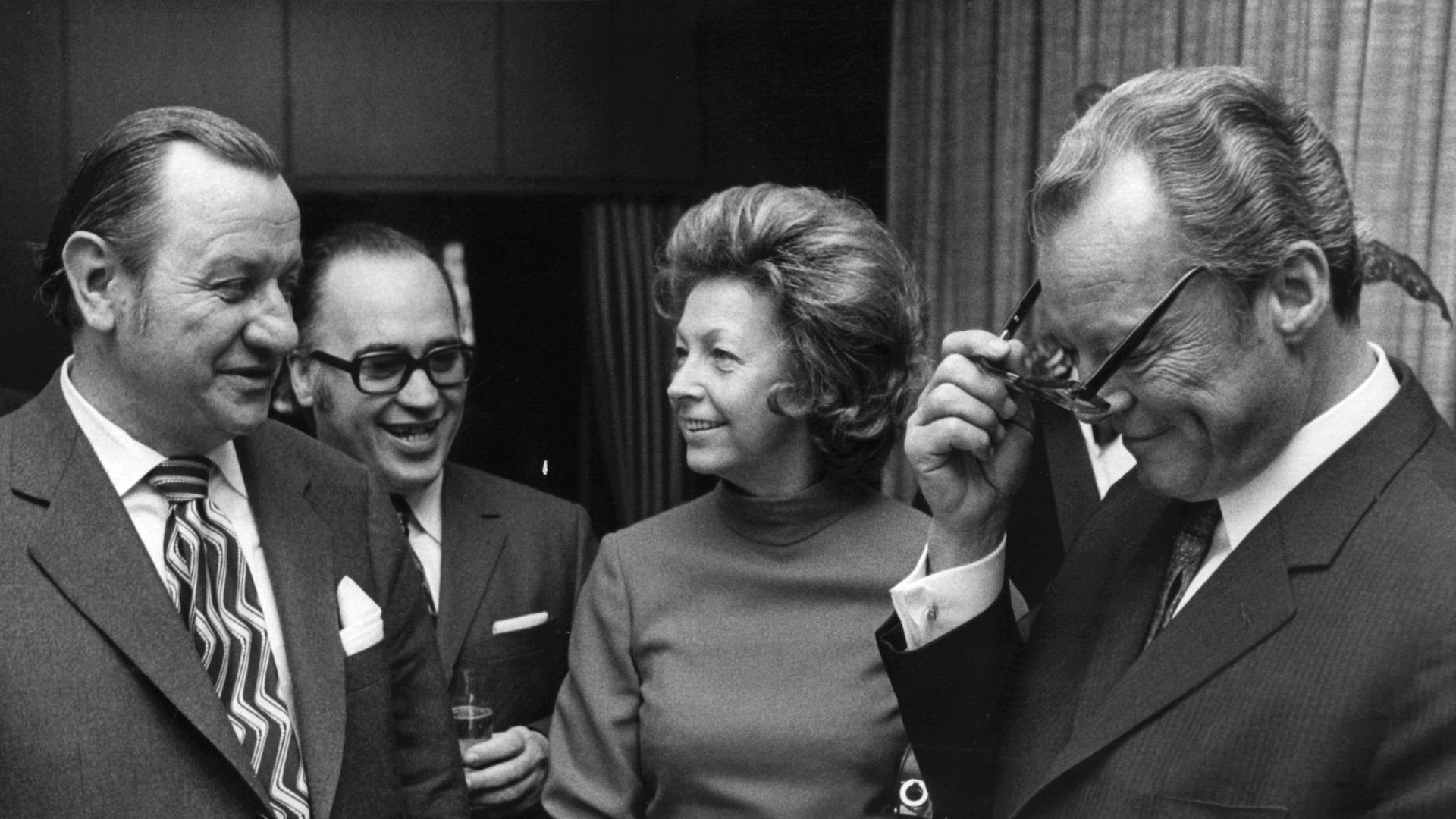 C. W. Ceram (links) präsentiert am 22. Februar 1972 dem damaligen Bundeskanzler Willy Brand sein neues Buch "Der erste Amerikaner". Zweiter von links, Joachim Raffert, Staatssekretär im Bundeswissenschaftsministerium. In der Bildmitte  Brandts Frau Rut