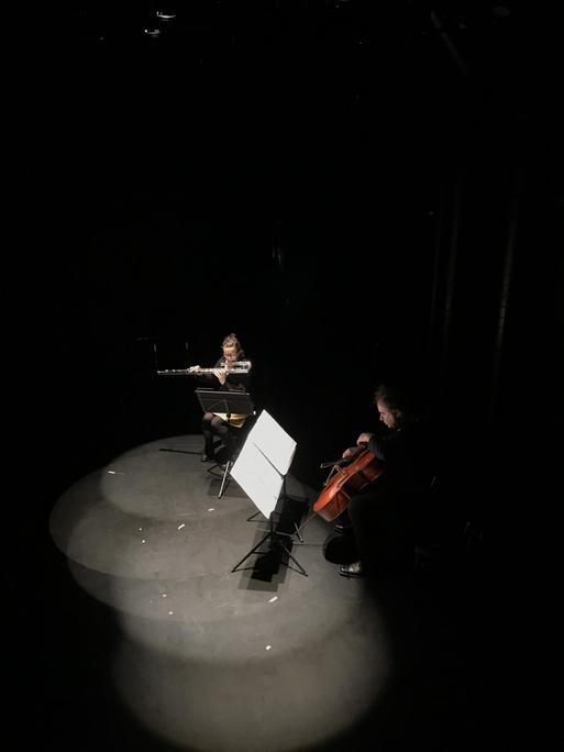 Zwei Musiker sitzen im Scheinwerferkegel auf einer dunklen Bühne