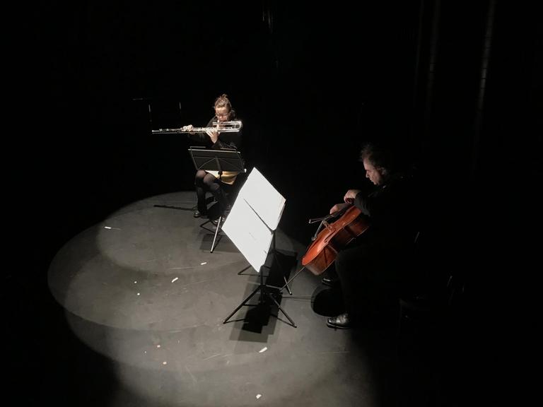 Zwei Musiker sitzen im Scheinwerferkegel auf einer dunklen Bühne