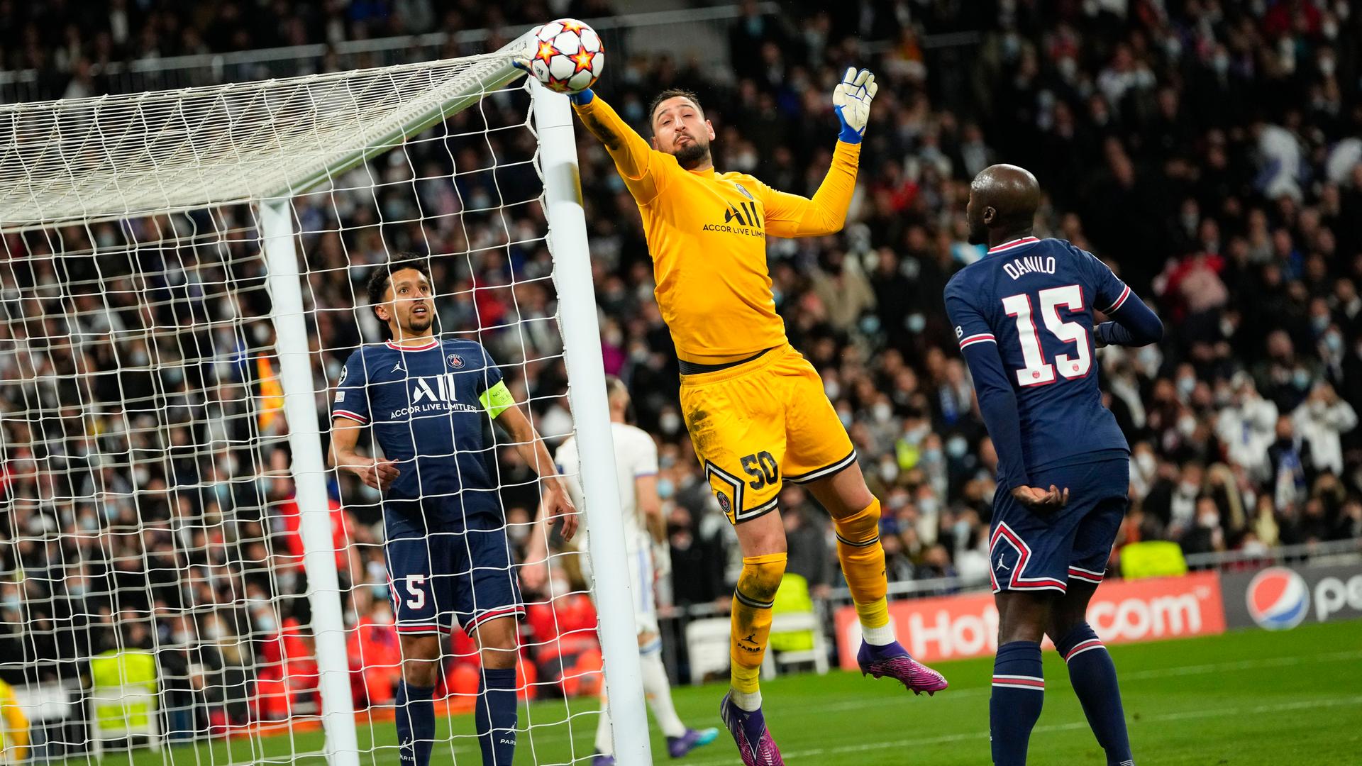 Torhüter Gianluigi Donnarumma springt an seinem Tor, um mit der rechten Hand einen Ball abzuwehren. Spieler von Real Madrid beobachten die Szene.