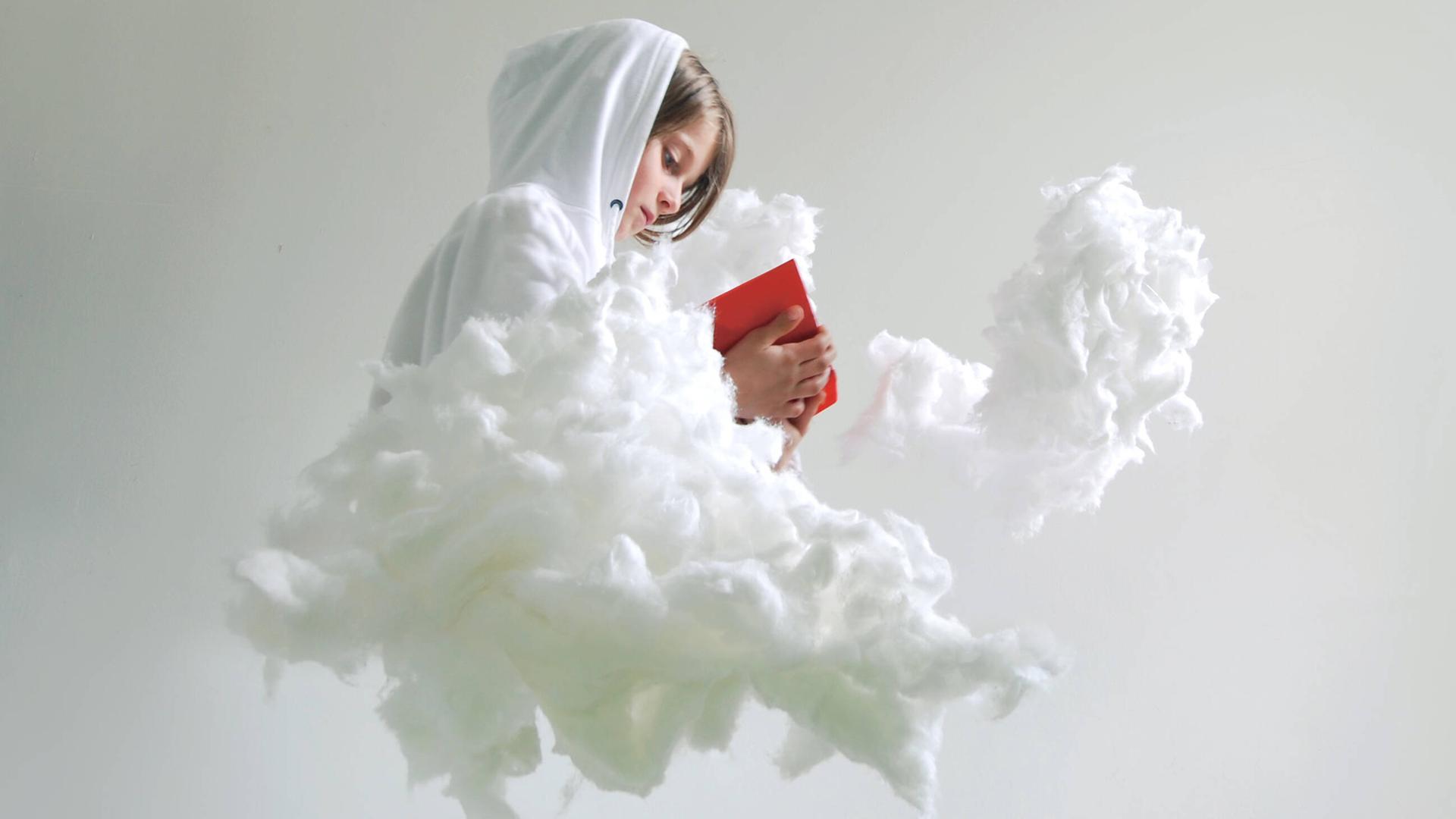 Ein Kind sitzt auf einer Wolke mit einem roten Buch in der Hand.