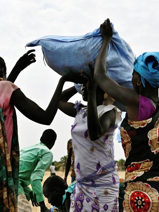 Frauen im Sudan tragen Hilfsgüter auf dem Kopf, Getreidesäcke aus dem Welternährungsprogramm.