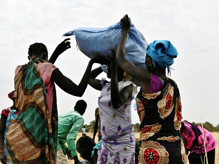 Frauen im Sudan tragen Hilfsgüter auf dem Kopf, Getreidesäcke aus dem Welternährungsprogramm.