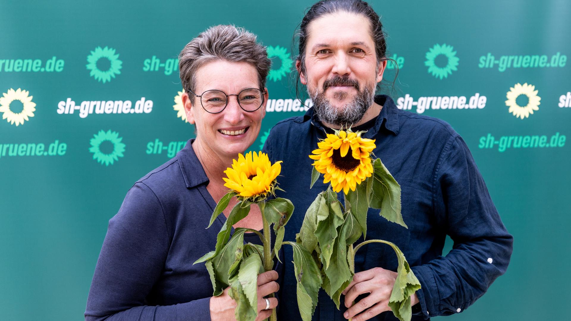 Anke Erdmann und Gazi Freitag stehen eng beieinander und halten Sonnenblumen in den Händen.